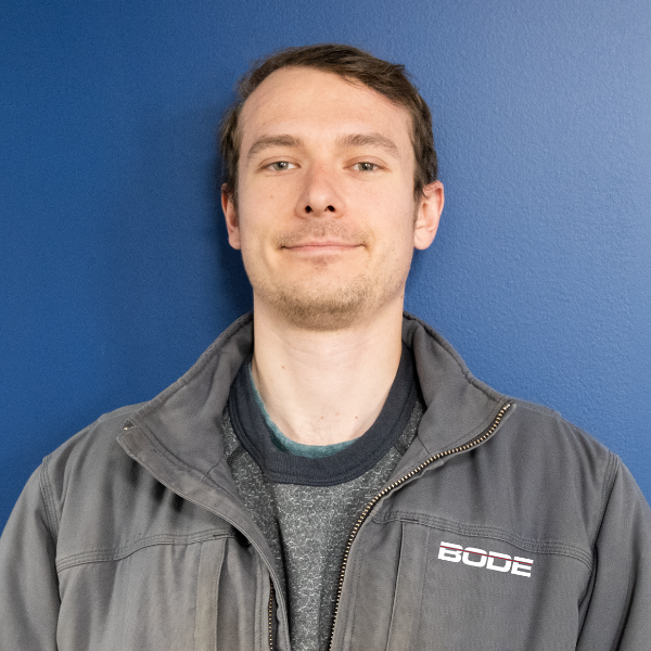 headshot of jacob mcadams with blue background and grey bode jacket