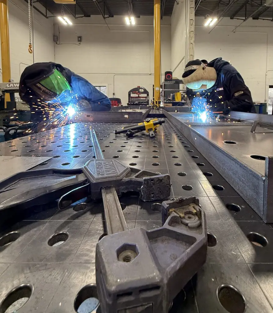 two welders welding worktables