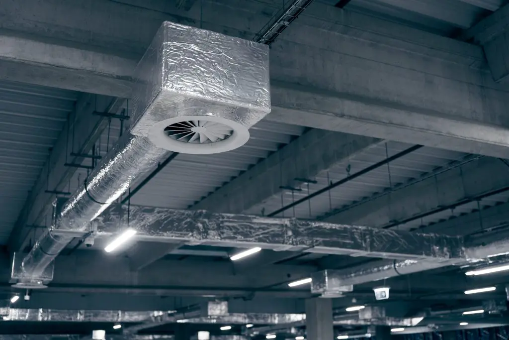 Air ventilation system on the ceiling in a large warehouse. Pipes made of silver insulating material hang from the ceiling inside the new building
